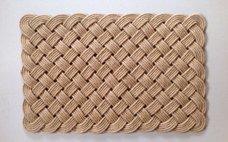 May include: A natural fiber doormat woven in a basket weave pattern with a decorative edge. The mat is beige in color.