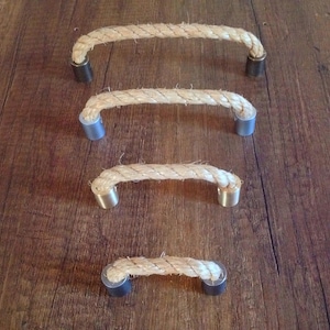 May include: Four drawer pulls arranged in a vertical line, each featuring a thick, natural-coloured twisted rope handle secured at both ends by cylindrical metal mounting brackets with a smooth, metallic finish and a flat circular base.