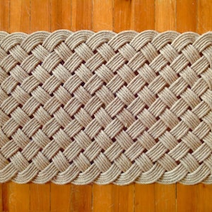 May include: A natural fiber doormat woven in a basket weave pattern with a rounded edge. The mat is made of thick, natural-colored rope.