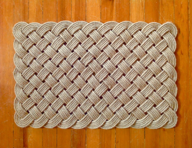 May include: A natural fiber doormat woven in a basket weave pattern with a rounded edge. The mat is made of thick, natural-colored rope.