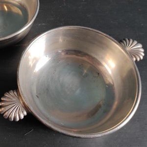 May include: Two silver bowls with scalloped handles. The bowls are empty and have a shiny finish.