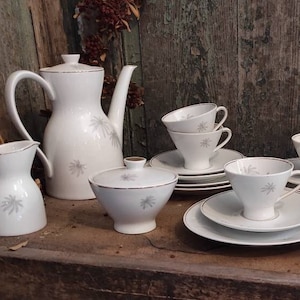 May include: A white porcelain tea set with a delicate floral pattern. The set includes a teapot, creamer, sugar bowl, and six cups and saucers.