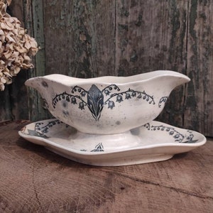 May include: A white ceramic gravy boat with a blue and white floral design. The boat has a scalloped edge and a footed base. It is sitting on a matching saucer.
