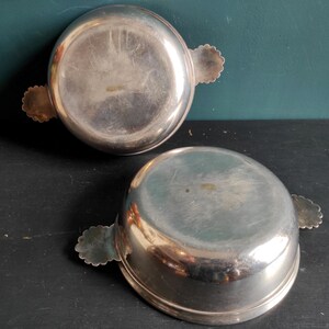 May include: Two silver serving dishes with ornate handles. The dishes are round and have a shiny finish.