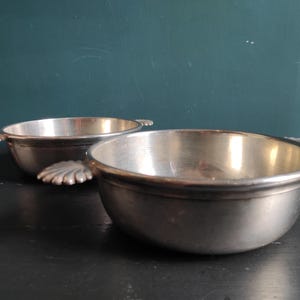 May include: Two silver bowls with handles in the shape of leaves. The bowls are on a black surface.