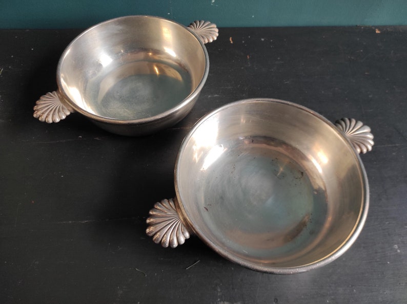 May include: Two silver bowls with scalloped handles. The bowls are empty and have a shiny finish.
