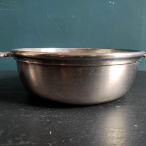 May include: A silver serving bowl with two handles. The bowl is round and has a smooth, shiny surface.
