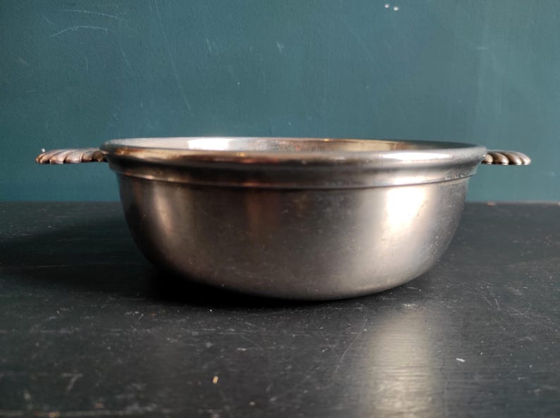 May include: A silver serving bowl with two handles. The bowl is round and has a smooth, shiny surface.