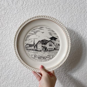 May include: A white ceramic plate with a gold rim features a black and white illustration of the University Methodist Church in Austin, Texas.