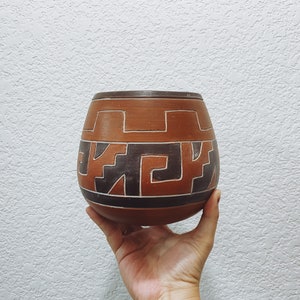 May include: A brown ceramic pot with a geometric design in black and white. The pot is hand-crafted and has a rounded shape.