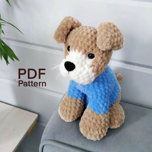 May include: Crochet pattern for a brown and white dog wearing a blue sweater. The pattern is available as a PDF download.