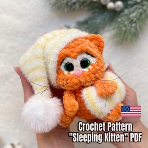 May include: An orange crochet kitten wearing a striped white and yellow hat and holding a heart-shaped pillow. The text "Crochet Pattern 'Sleeping Kitten' PDF" is displayed below the kitten.