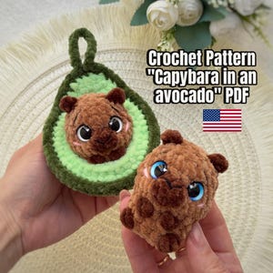 May include: A brown crocheted capybara plush toy and a separate crocheted avocado-shaped holder with a capybara inside. The text reads Crochet Pattern "Capybara in an avocado" PDF. The items are made of soft, textured yarn with small plastic eyes.