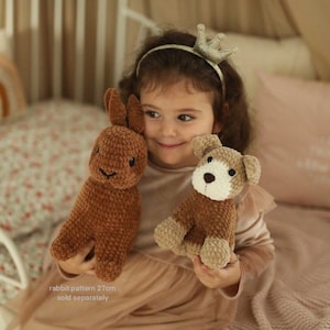May include: A young child wearing a crown headband holds a brown crocheted rabbit and a brown crocheted dog. The rabbit is 27 cm tall and is sold separately.