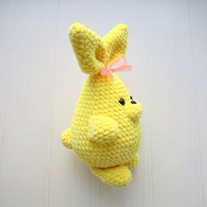 Op de afbeelding: Een gele gehaakte bunny met een roze strik. De bunny heeft zwarte ogen en een kleine neus.