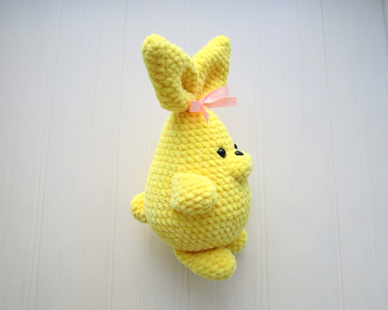 Op de afbeelding: Een gele gehaakte bunny met een roze strik. De bunny heeft zwarte ogen en een kleine neus.