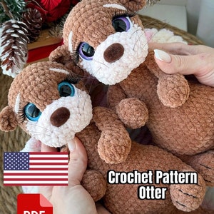 May include: Crochet pattern for an otter amigurumi toy. The pattern is available as a PDF download. The image shows two brown and white crocheted otters with big blue eyes and long eyelashes.