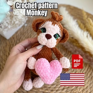 Könnte beinhalten: Häkelanleitung für einen braunen Affen, der ein rosa Herz hält. Das Muster ist als PDF-Download erhältlich. Das Bild enthält den Text "Crochet pattern Monkey" und eine US-Flagge.