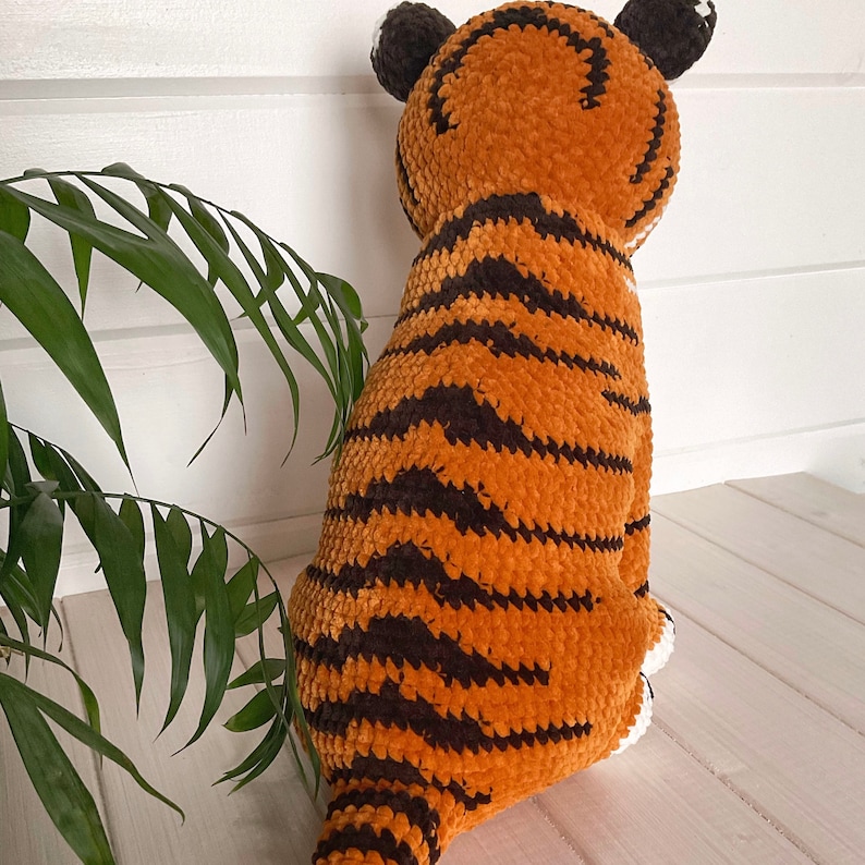 Puede incluir: Un peluche de tigre, principalmente naranja con rayas marrones oscuras. El tigre tiene orejas marrones oscuras y detalles blancos. El juguete est&aacute; hecho de un material suave y texturizado y est&aacute; sentado sobre una superficie clara.
