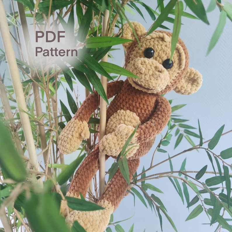 K&ouml;nnte beinhalten: Ein geh&auml;keltes Affenspielzeug mit braunem und beigefarbenem Fell, das auf einem Ast sitzt. Der Affe hat einen freundlichen Ausdruck und h&auml;lt sich mit seinen H&auml;nden am Ast fest. Der Text "PDF Pattern" ist im Bild sichtbar.
