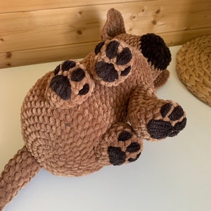 May include: A brown crocheted plush dog toy with black paw prints. The dog is lying on its back with its legs in the air.