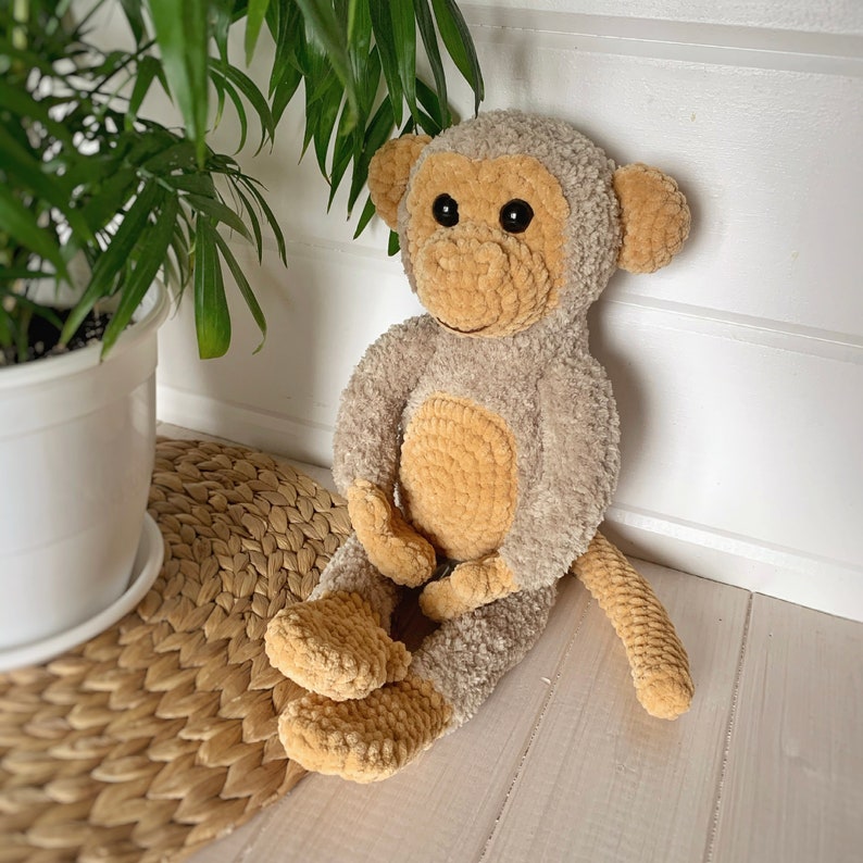 K&ouml;nnte beinhalten: Ein geh&auml;keltes Affenspielzeug in beige und braunen Farben. Der Affe sitzt auf einer geflochtenen Strohmatte.