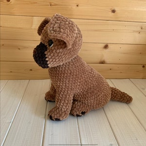 May include: A brown crocheted plush dog toy with black eyes and a black nose. The dog is sitting with its tail curled to the side.