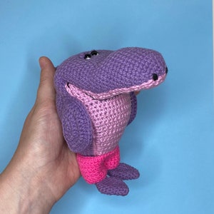 K&ouml;nnte beinhalten: Ein geh&auml;keltes lila und pinkfarbenes Nilpferd-Spielzeug mit schwarzen Augen. Das Nilpferd tr&auml;gt eine rosa Shorts.
