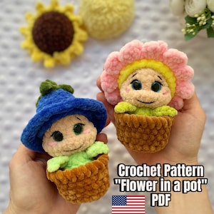 Puede incluir: Dos muñecas de flores de ganchillo hechas a mano en macetas marrones, una con un sombrero azul y la otra con una corona de flores rosas. Un girasol amarillo y una bola amarilla están en el fondo. El texto "Crochet Pattern 'Flower in a pot' PDF" es visible.