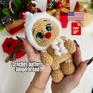 May include: A crocheted gingerbread man doll with a white hood and scarf, green eyes, and a red nose. The doll is held in a person's hands. The text "Crochet pattern Gingerbread" is visible.