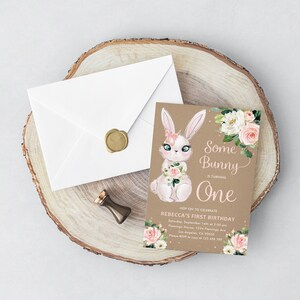 May include: A brown invitation card with a white bunny illustration holding pink flowers. The text reads "Some Bunny is turning One. Hop on to celebrate Rebecca's First Birthday. Saturday, September 14th at 2:00 pm. Flamingo House, 1234 Flamingo Ave. Los Angeles, CA 90055. Please RSVP to Lucy at 123 456 789."