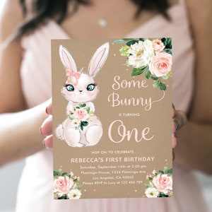 May include: A brown paper invitation with a pink and white floral design. The invitation features a cartoon bunny with a pink bow and the text "Some Bunny is Turning One". The invitation also includes the text "Hop on to Celebrate Rebecca's First Birthday" and details for the event.