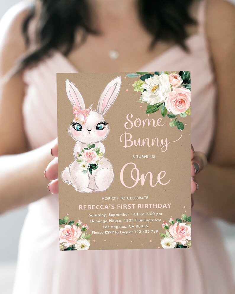 May include: A brown paper invitation with a pink and white floral design. The invitation features a cartoon bunny with a pink bow and the text "Some Bunny is Turning One". The invitation also includes the text "Hop on to Celebrate Rebecca's First Birthday" and details for the event.
