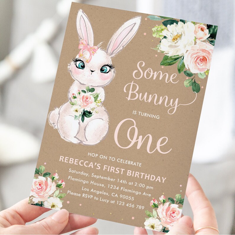 May include: A brown paper card with a white bunny holding pink flowers. The card has the text "Some Bunny is Turning One" and details for a first birthday party.