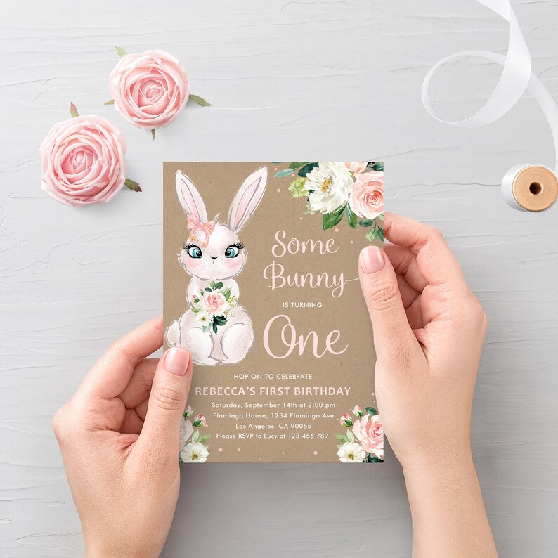 May include: A brown invitation card with a white bunny illustration and pink floral accents. The text reads "Some Bunny is turning One" and includes details for a first birthday party.