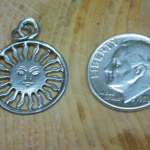 May include: Silver pendant charm featuring a sun with a face and rays. The pendant is about the size of a ten pence piece.