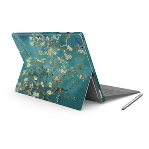 May include: A teal laptop with a floral design on the back. The laptop is closed and the screen is facing away from the viewer. A stylus is lying on the table next to the laptop.