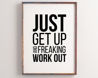 May include: A framed motivational poster with the text "JUST GET UP AND FREAKING WORK OUT" hanging on a white wall above a wooden table with two stools. The table has a stack of books and a white coffee cup on a saucer.