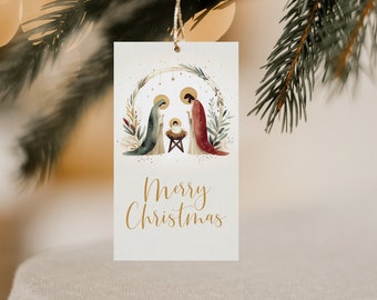 Può includere: Un'etichetta regalo natalizia rettangolare con un'illustrazione ad acquerello della scena della Natività, con Maria, Giuseppe e Gesù bambino. L'etichetta riporta la scritta "Merry Christmas" in oro ed è appesa a un filo d'oro.