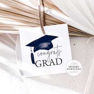 May include: A white printable gift tag with a blue graduation cap and the text "congrats GRAD". The tag is tied with a brown string and has a small circle with the text "INSTANT DOWNLOAD" in the bottom right corner.