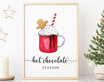 May include: A framed print featuring a watercolor illustration of a red mug of hot chocolate with whipped cream, a gingerbread man, and a striped straw. The text "hot chocolate station" is below the mug. A small Christmas tree and gold star decorations are in the background.