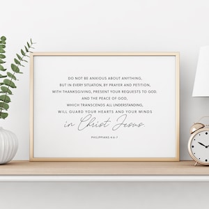 Puede incluir: Una impresi&oacute;n enmarcada con un marco dorado muestra el texto "DO NOT BE ANXIOUS ABOUT ANYTHING...in Christ Jesus." La impresi&oacute;n est&aacute; sobre un fondo blanco. Un peque&ntilde;o despertador dorado y vegetaci&oacute;n est&aacute;n en el estante.