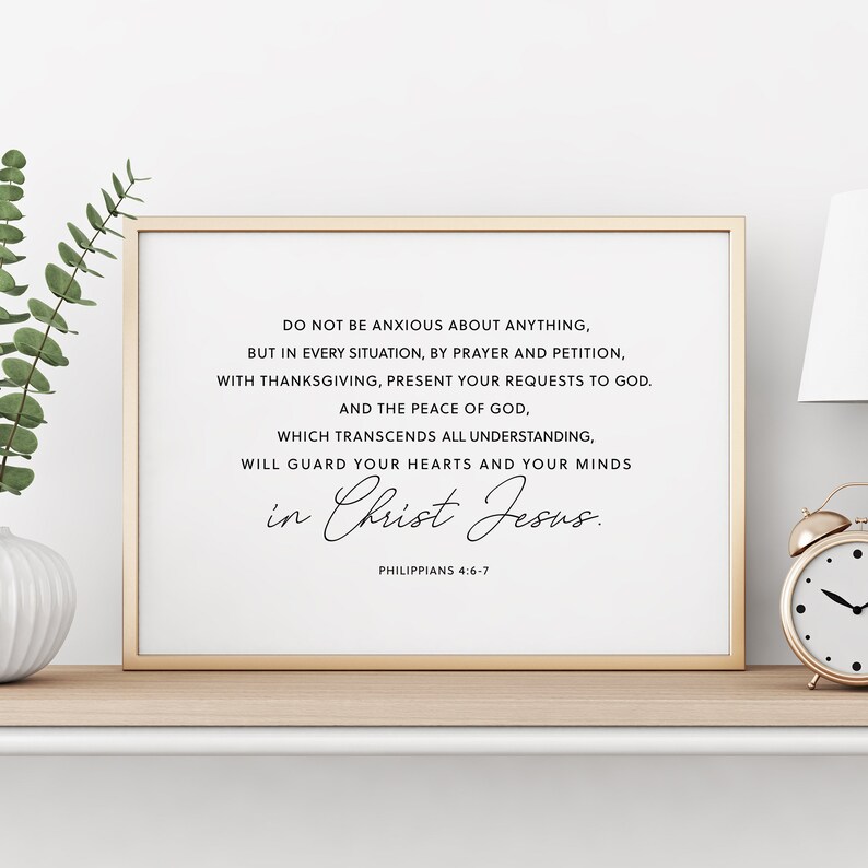 Puede incluir: Una impresi&oacute;n enmarcada con un marco dorado muestra el texto "DO NOT BE ANXIOUS ABOUT ANYTHING...in Christ Jesus." La impresi&oacute;n est&aacute; sobre un fondo blanco. Un peque&ntilde;o despertador dorado y vegetaci&oacute;n est&aacute;n en el estante.