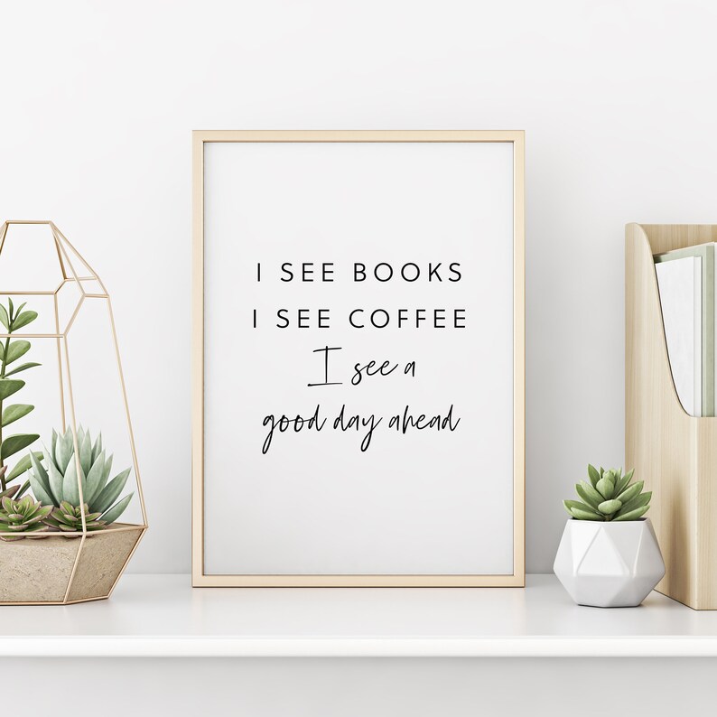 Op de afbeelding: Een ingelijst print met de tekst "I see books I see coffee I see a good day ahead" in zwarte schrijfletters op een witte achtergrond.