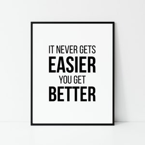 Puede incluir: Una impresión enmarcada con la cita motivacional, "IT NEVER GETS EASIER YOU GET BETTER", en texto negro en negrita sobre un fondo blanco. La impresión está dentro de un marco negro, adecuada para la decoración del hogar.