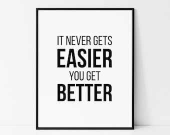 May include: A framed print with the motivational quote, "IT NEVER GETS EASIER YOU GET BETTER," in bold black text on a white background. The print is encased in a black frame, suitable for home or office decor.