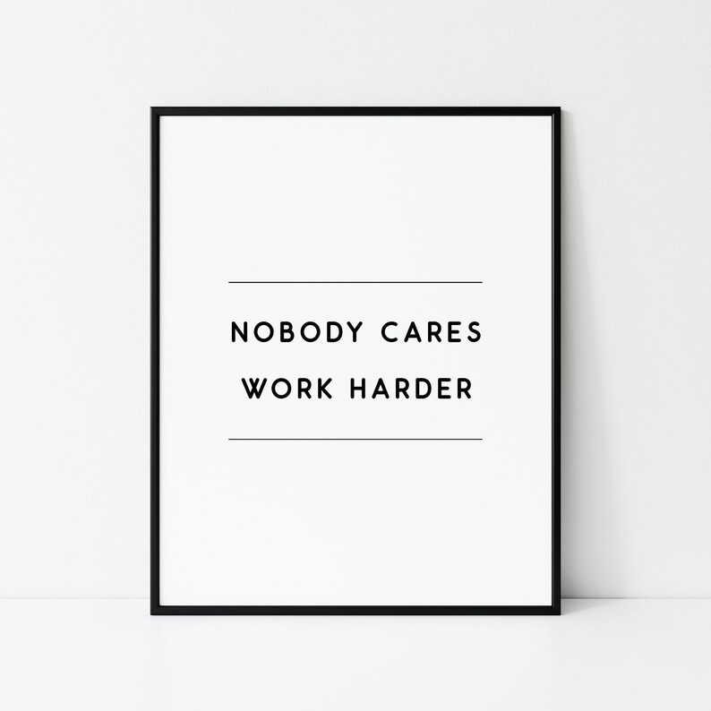 May include: A framed print with the text "NOBODY CARES WORK HARDER" in black, centered on a white background. The print is enclosed in a black frame, suitable for home or office decor.