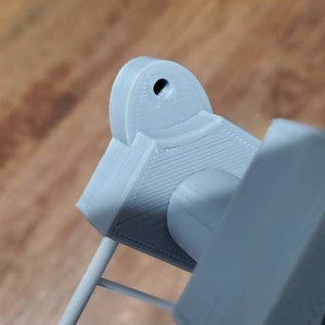 May include: A gray 3D printed object with a round hole in the top. The object is attached to a gray metal frame.