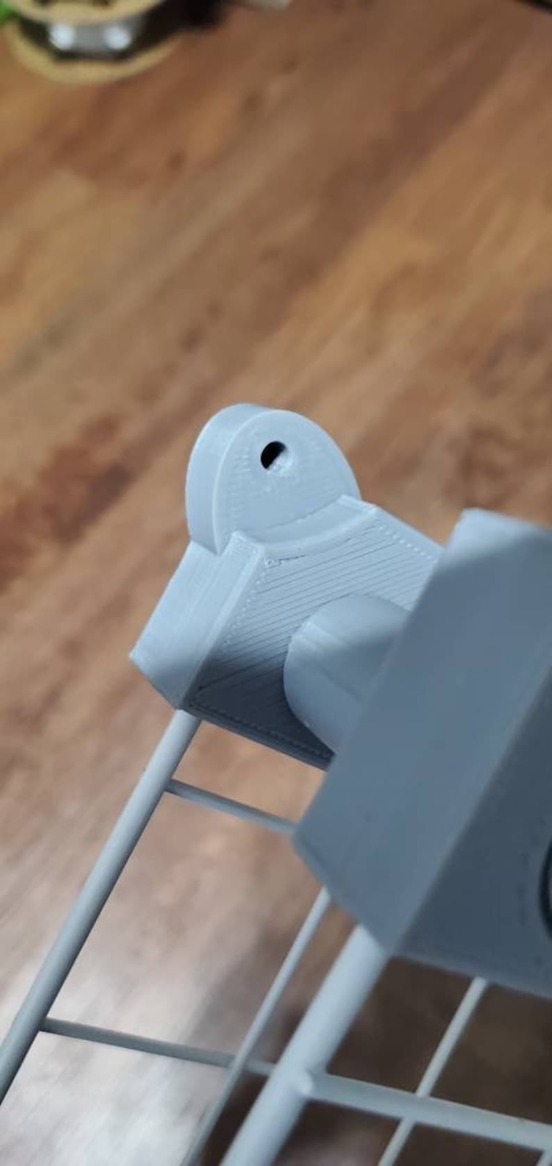 May include: A gray 3D printed object with a round hole in the top. The object is attached to a gray metal frame.