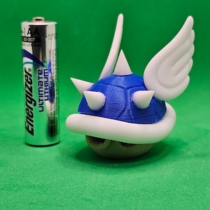 May include: A blue and white 3D printed figurine of a winged Koopa Troopa from the Super Mario Bros. video game series. The figurine is about the size of a AA battery.